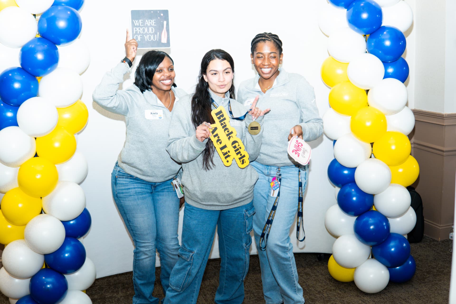 Three guests posing with props between blue, yellow and white balloon columns